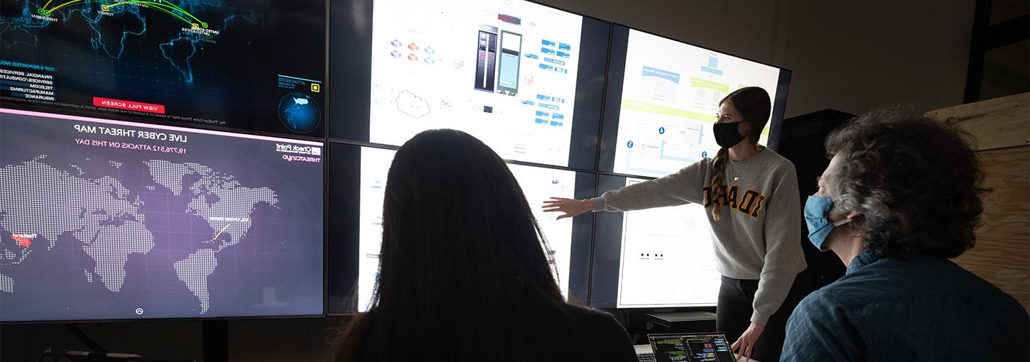 Woman touching multi-media display with two individuals seated.